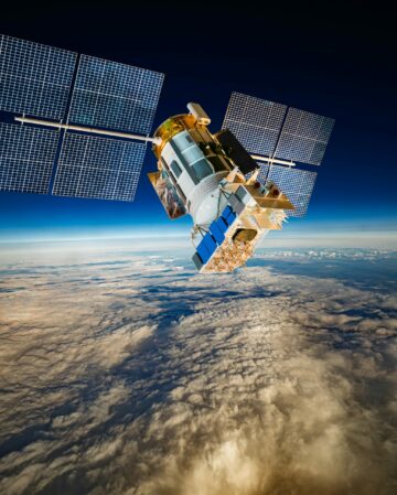 Detailed view of a satellite in space, featuring metallic structure, antennas, and large solar panels, orbiting above Earth's blue atmosphere and orange-tinted cloud layers against the dark void.